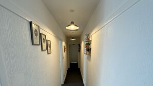 A hallway with framed certificates on the walls, a ceiling light, and a door at the end. - Two Bedroom - Apartment (Skegness)