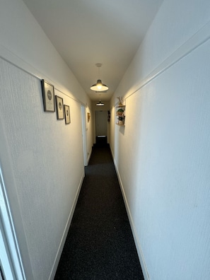 A hallway with framed certificates on the walls, a ceiling light, and a door at the end. - Two Bedroom - Apartment (Skegness)