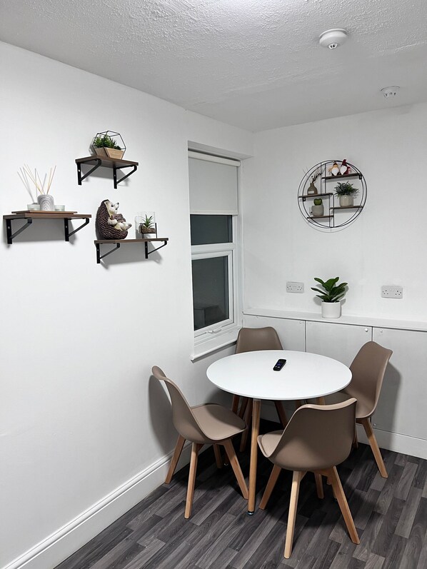 A room with a round table and four chairs, a window, and wall-mounted shelves with plants and decorative items.