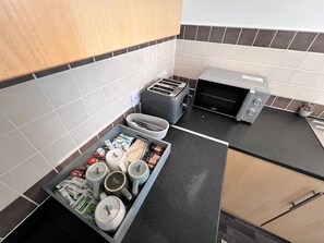 Une cuisine équipée d’un grille-pain, d’un four à micro-ondes et d’un tiroir contenant des ustensiles et des tasses.