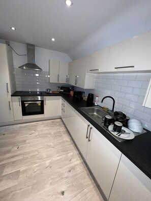 A modern kitchen with white cabinets, a black countertop, and a stainless steel range hood. - Duplex Family Apartment (Skegness)