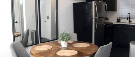 A modern kitchen with a black refrigerator, stainless steel appliances, and a wooden dining table with four grey chairs.