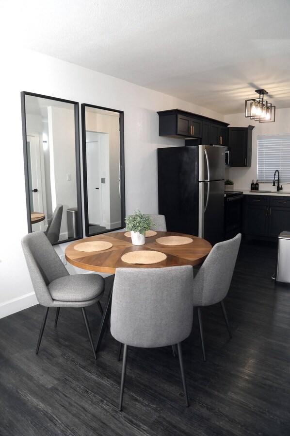 A modern kitchen with a black refrigerator, stainless steel appliances, and a wooden dining table with four grey chairs.