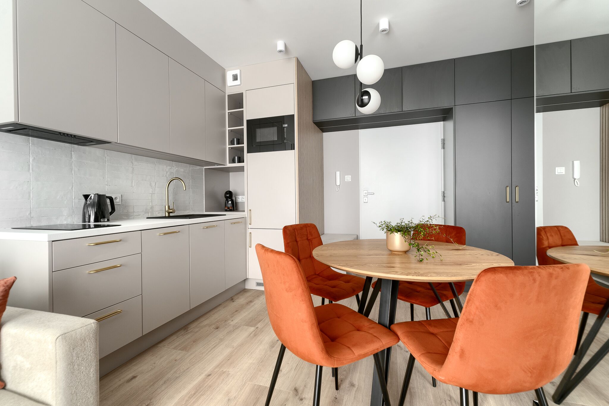 Una cocina moderna con armarios grises, un microondas negro y una mesa de comedor redonda de madera con sillas naranjas.