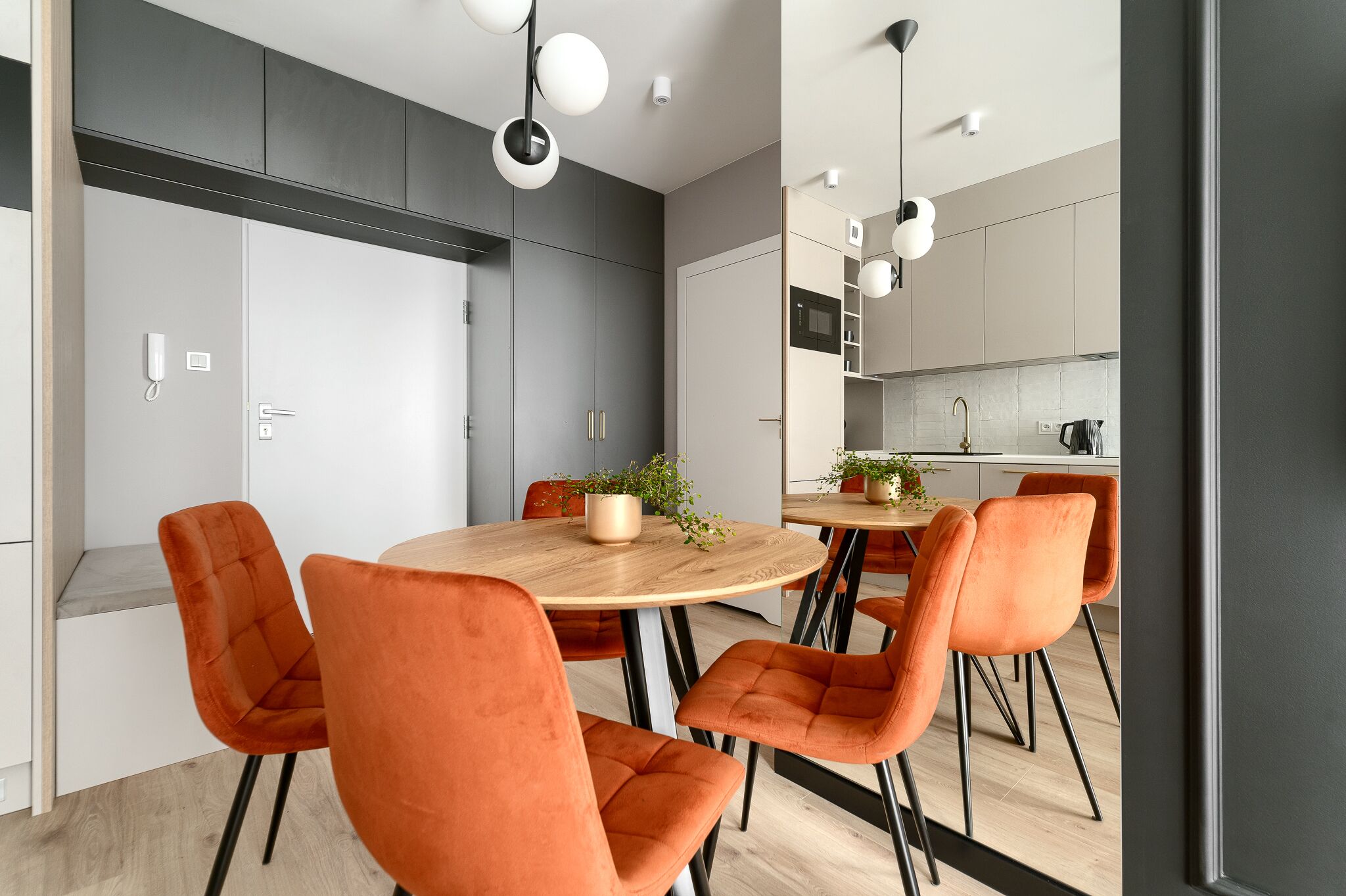 Una cocina moderna con una isla central, armarios blancos y un comedor con sillas naranjas.