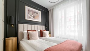 Um quarto moderno com uma cama grande, duas mesas de cabeceira, um criado-mudo redondo de madeira e uma pintura abstrata emoldurada na parede.