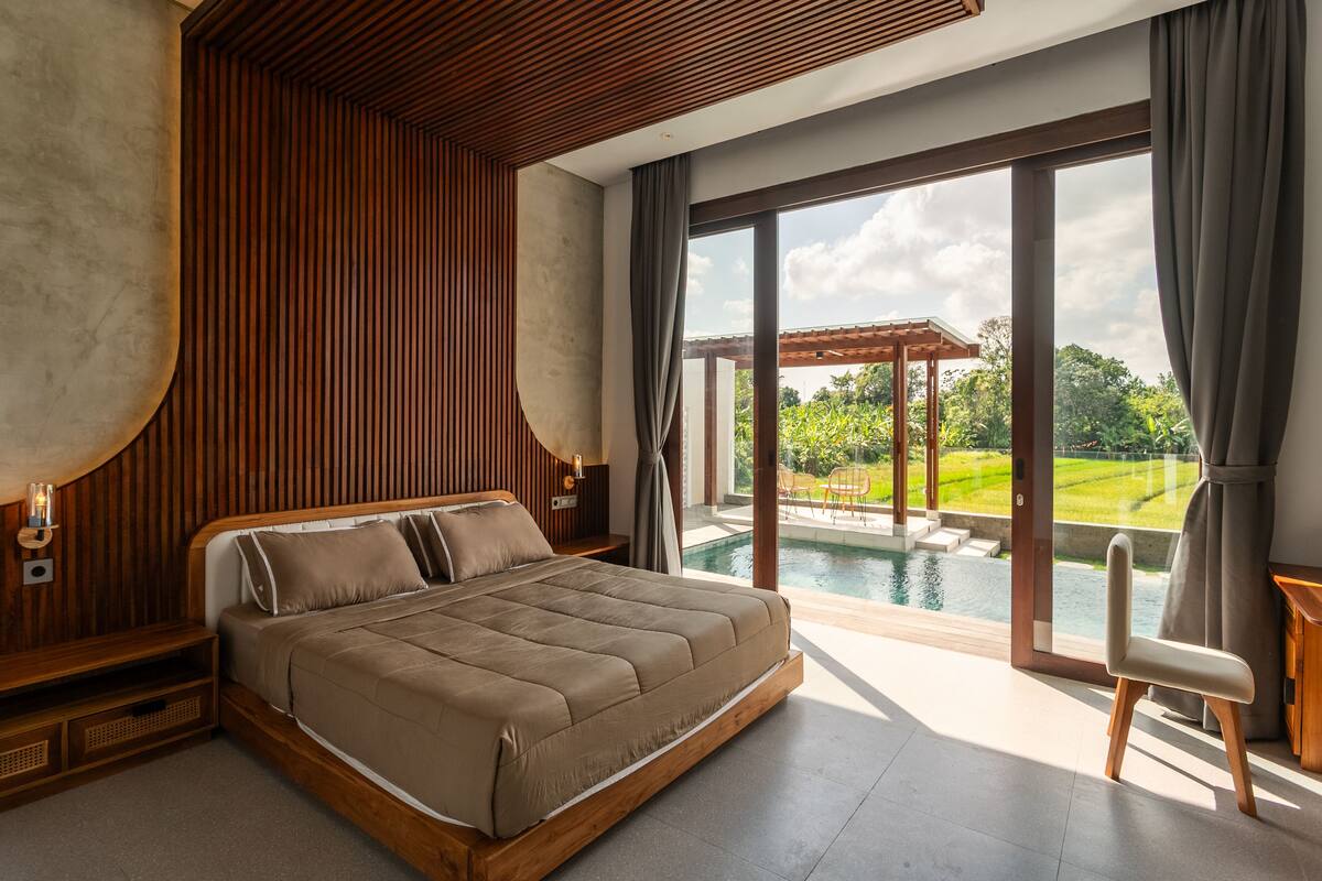 A modern bedroom with a large bed, a view of a swimming pool, and a pergola outside.