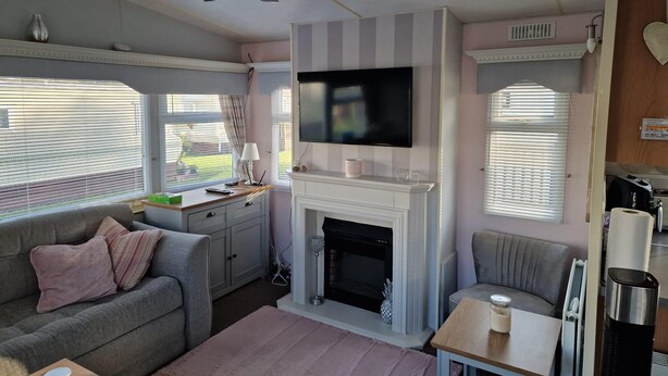 A cozy living room with a fireplace, a television mounted above it, and a comfortable seating area with a sofa and a table. - Lovely pet Friendly 4 Berth Caravan in Morecambe (Morecambe)