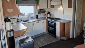A compact kitchen with a gas stove, sink, and white cabinets. - Lovely pet Friendly 4 Berth Caravan in Morecambe (Morecambe)