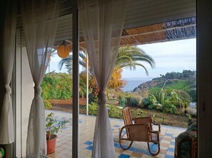 A room with a view of a coastal landscape, a wicker chair, and a potted plant.
