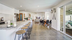 A modern kitchen with a marble countertop, bar stools, and a dining area with a glass table and chairs.