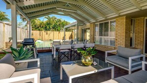 An outdoor patio with a covered seating area, a pool, and a brick wall.