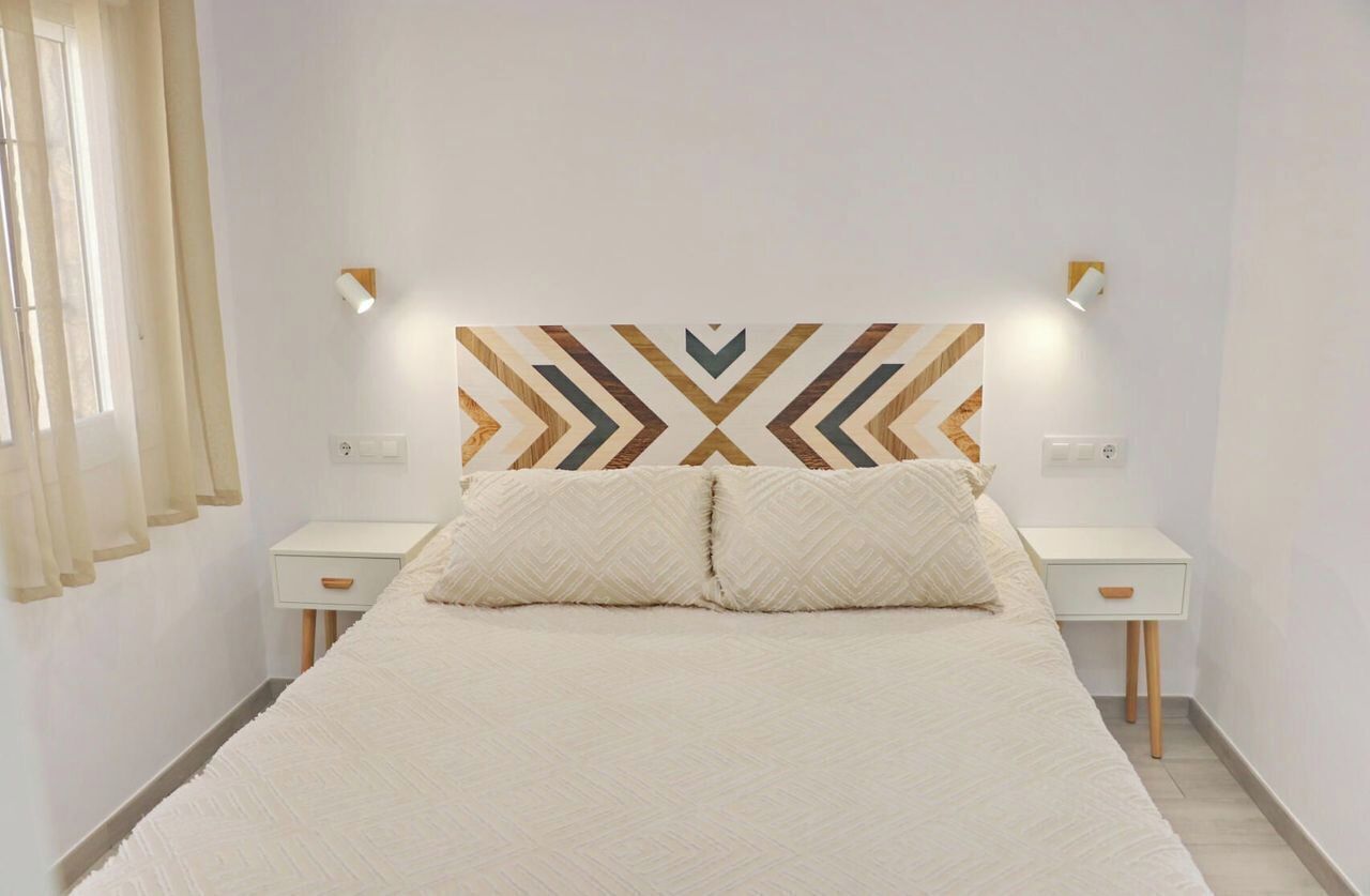 A bedroom with a bed, two bedside tables, and a geometric-patterned headboard.