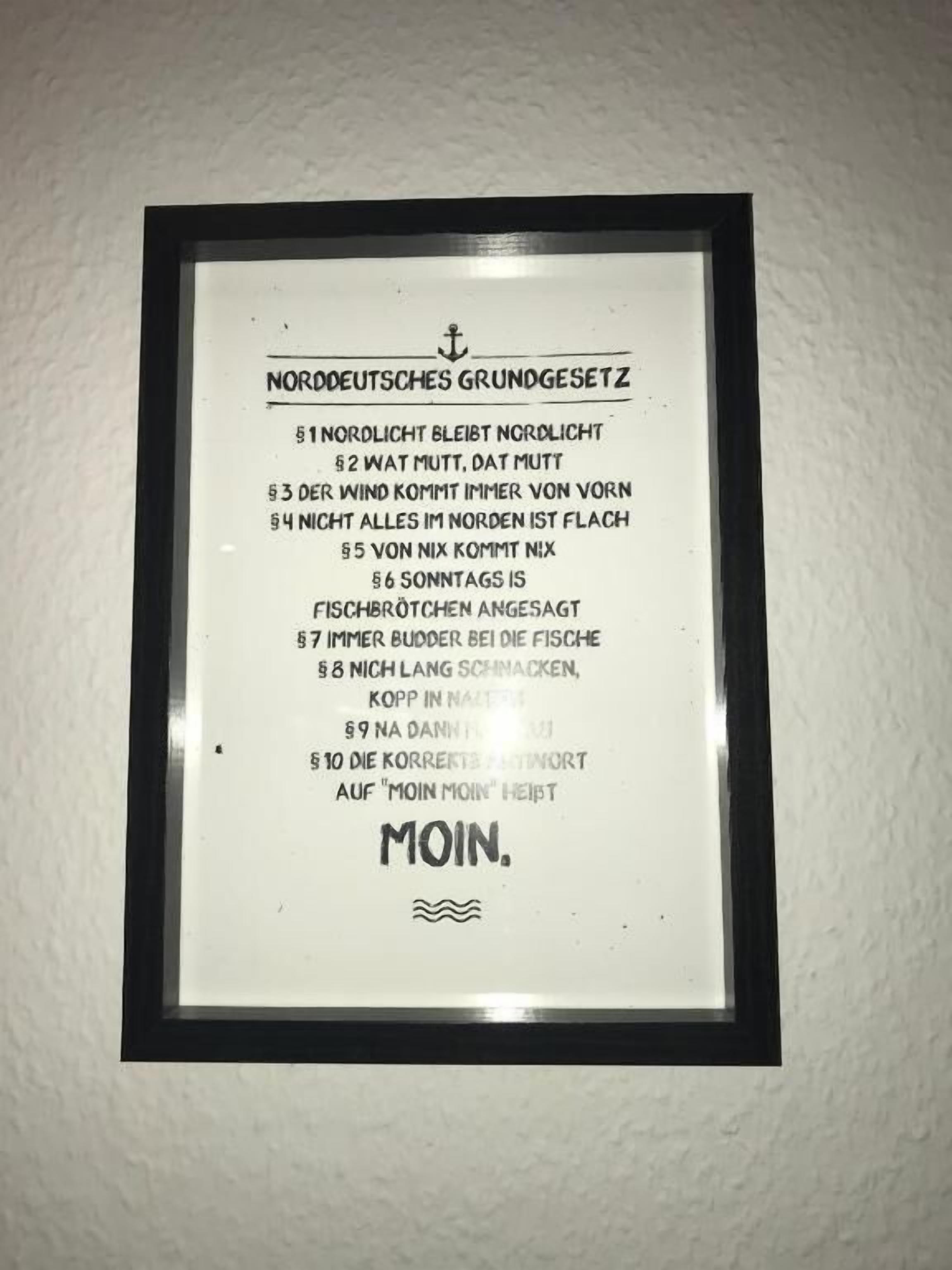 A framed sign with text in German, likely related to a location or event, mounted on a wall.