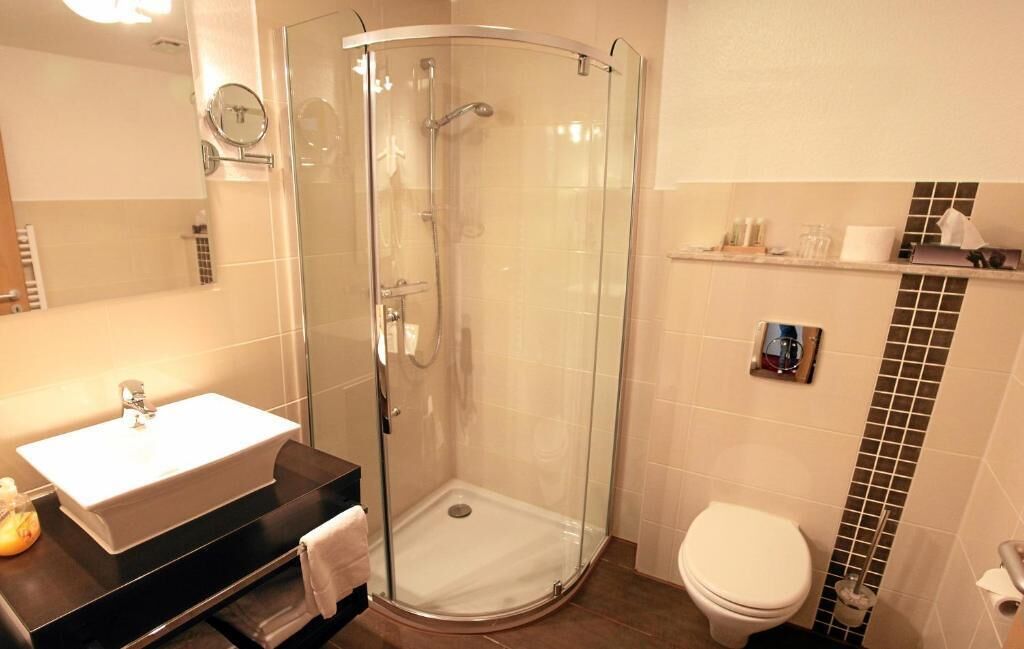 A modern bathroom with a glass-enclosed shower, a white sink, and a toilet.