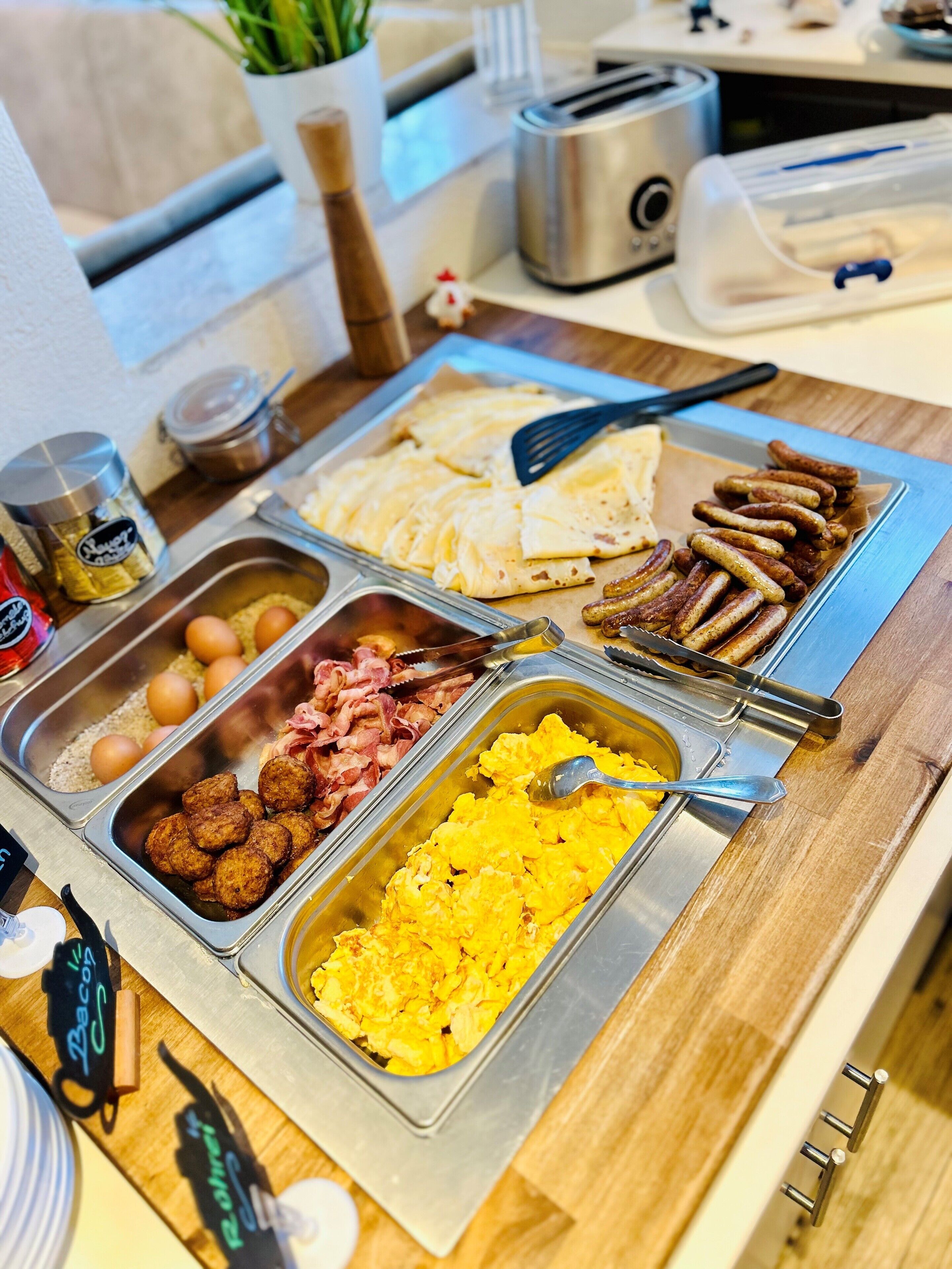A buffet with various food options including eggs, bacon, sausages, and scrambled eggs.