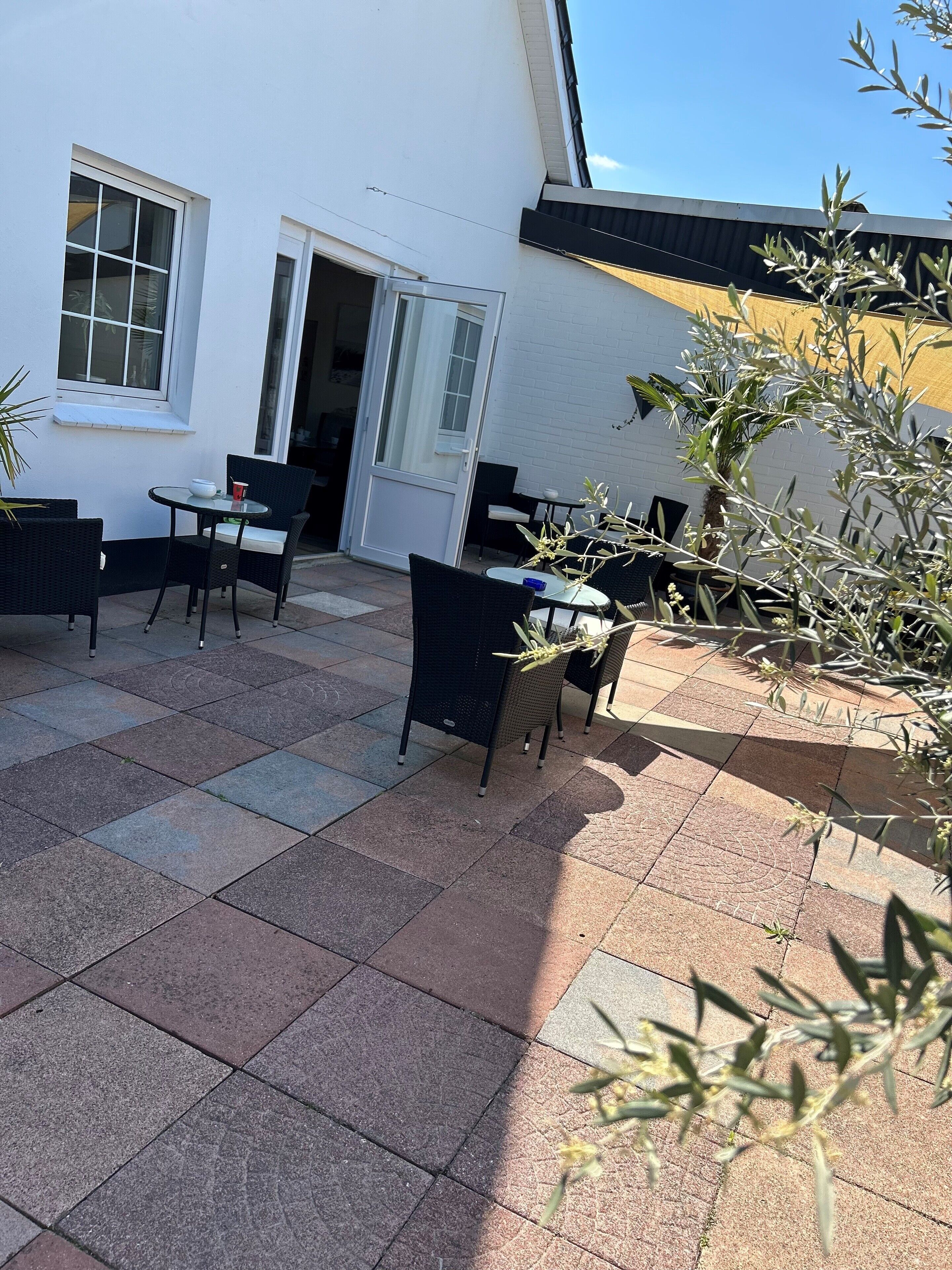 A patio with outdoor seating, a white building, and a door leading to an interior space.