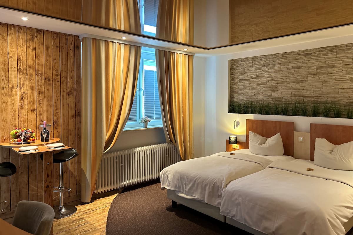 A hotel room with a wooden wall, a bed with white bedding, a desk with a chair, and a radiator.