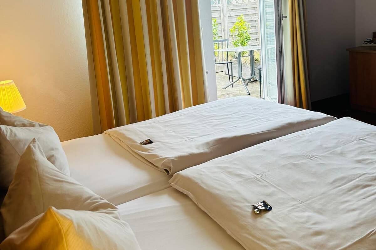 A hotel room with two beds, a sofa, a lamp, and a view of the outside.