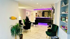 A hotel lobby with a reception desk, seating area, and a bookshelf. - Tauwerk Hotel (Wilhelmshaven)