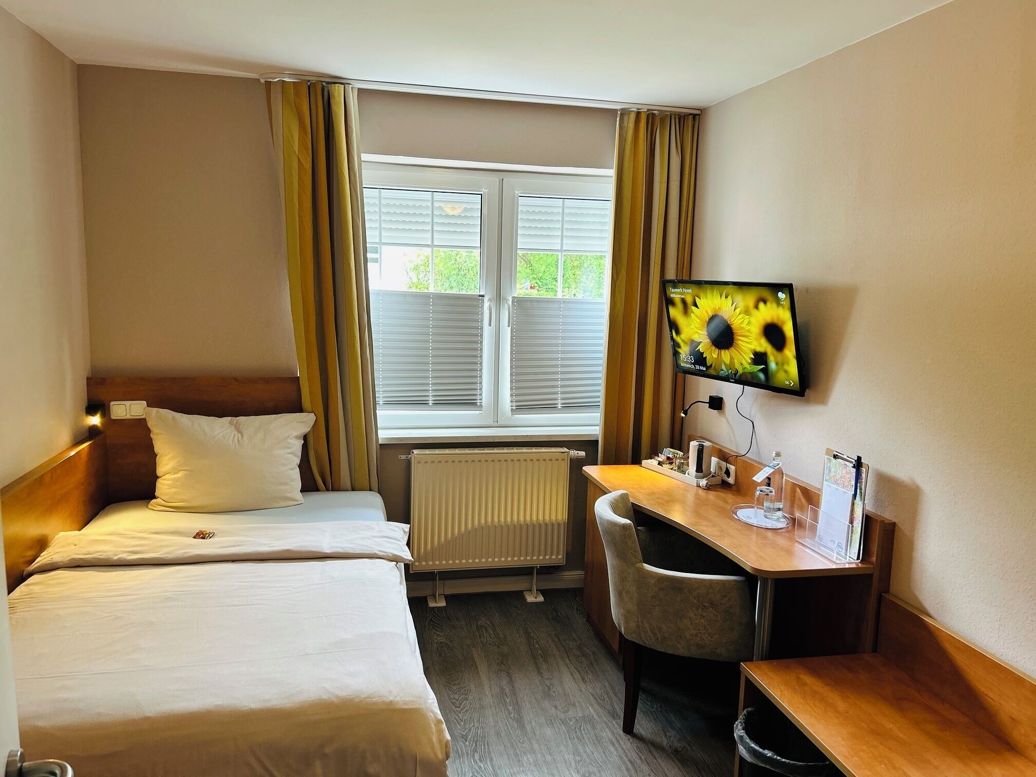 Une chambre d’hôtel avec deux lits, un bureau, une chaise, une télévision et une fenêtre avec des rideaux.