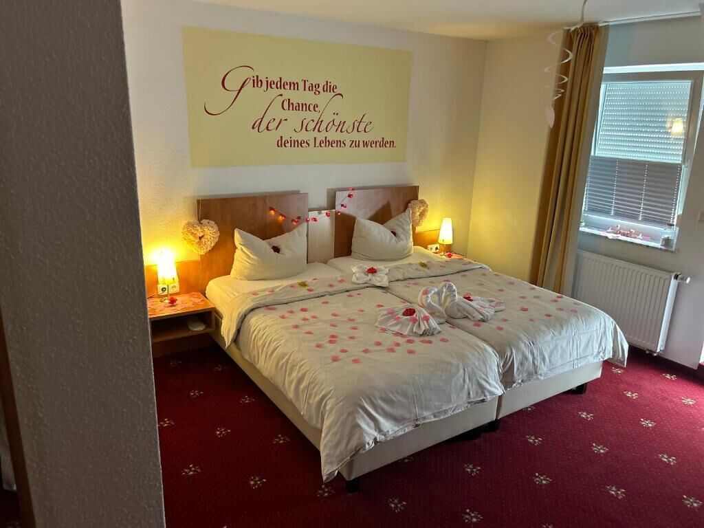 A neatly made bed with white linens and pink floral patterns, two bedside lamps, and a wall with a motivational quote.
