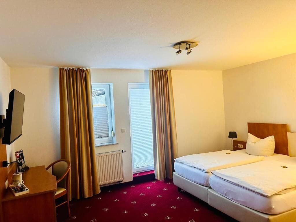 A hotel room with two beds, a desk with a chair, a TV, and a window with curtains.