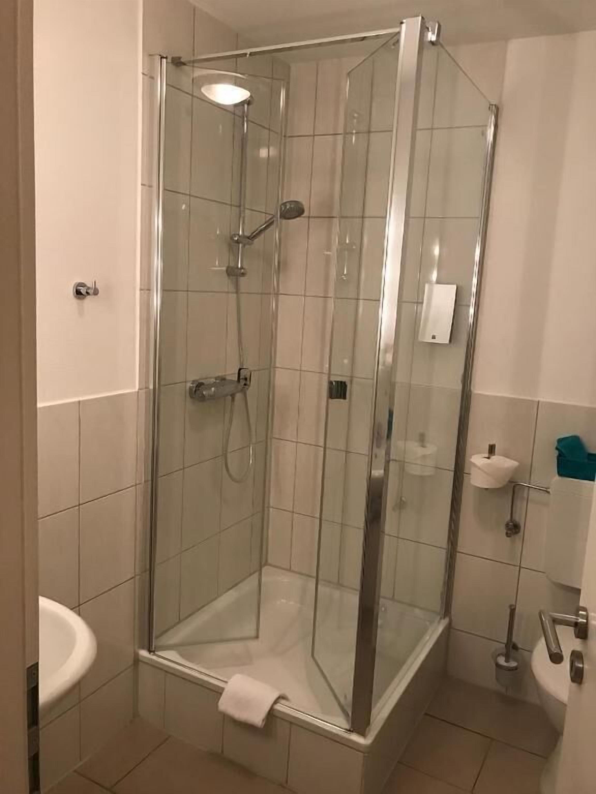 A glass-enclosed shower with a handheld showerhead, a handheld showerhead, and a handheld showerhead.