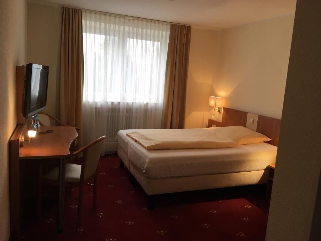 A hotel room with a bed, a desk, a chair, a television, and a window with curtains.