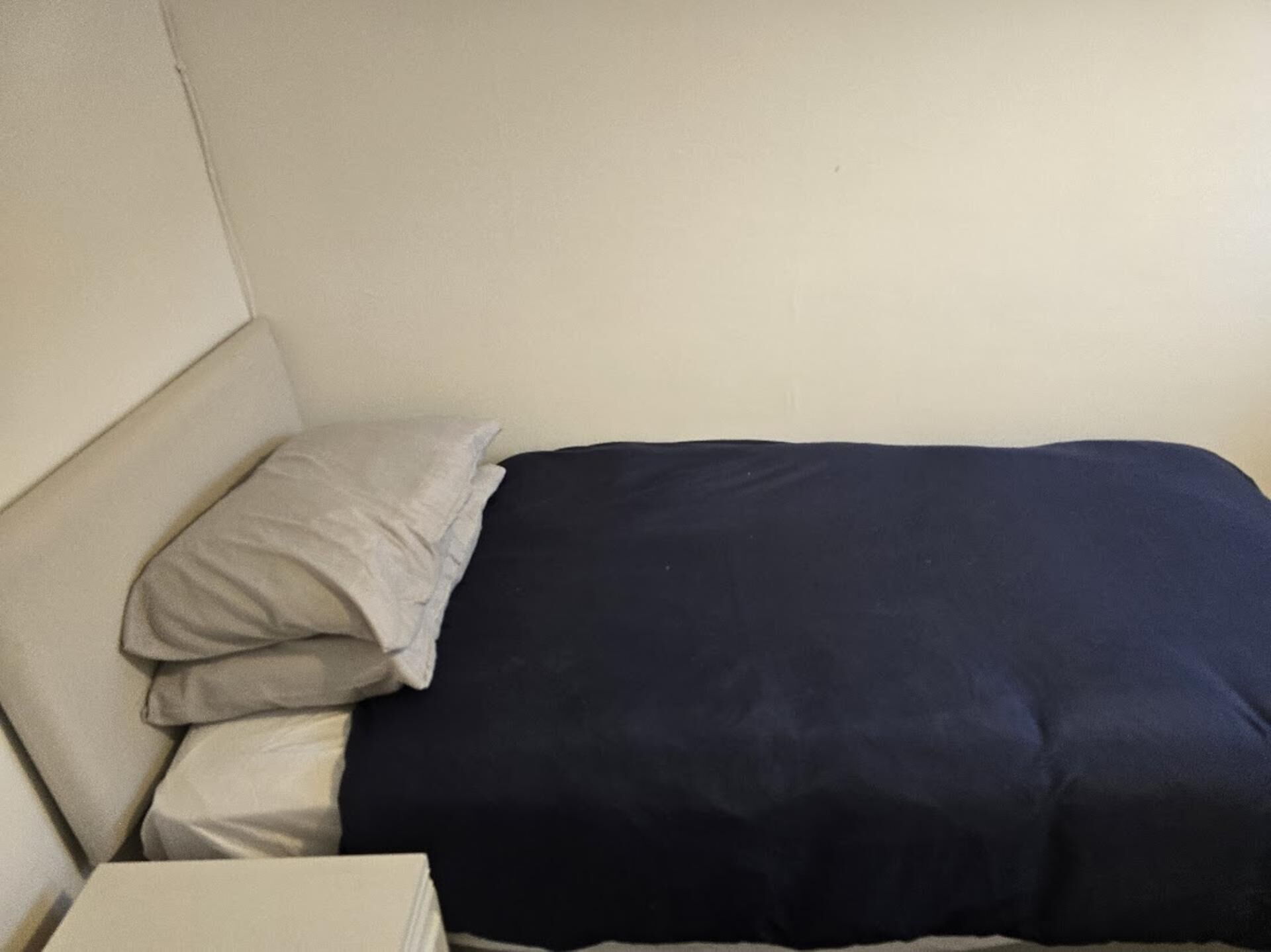 Cama com colcha azul escura e travesseiro claro.