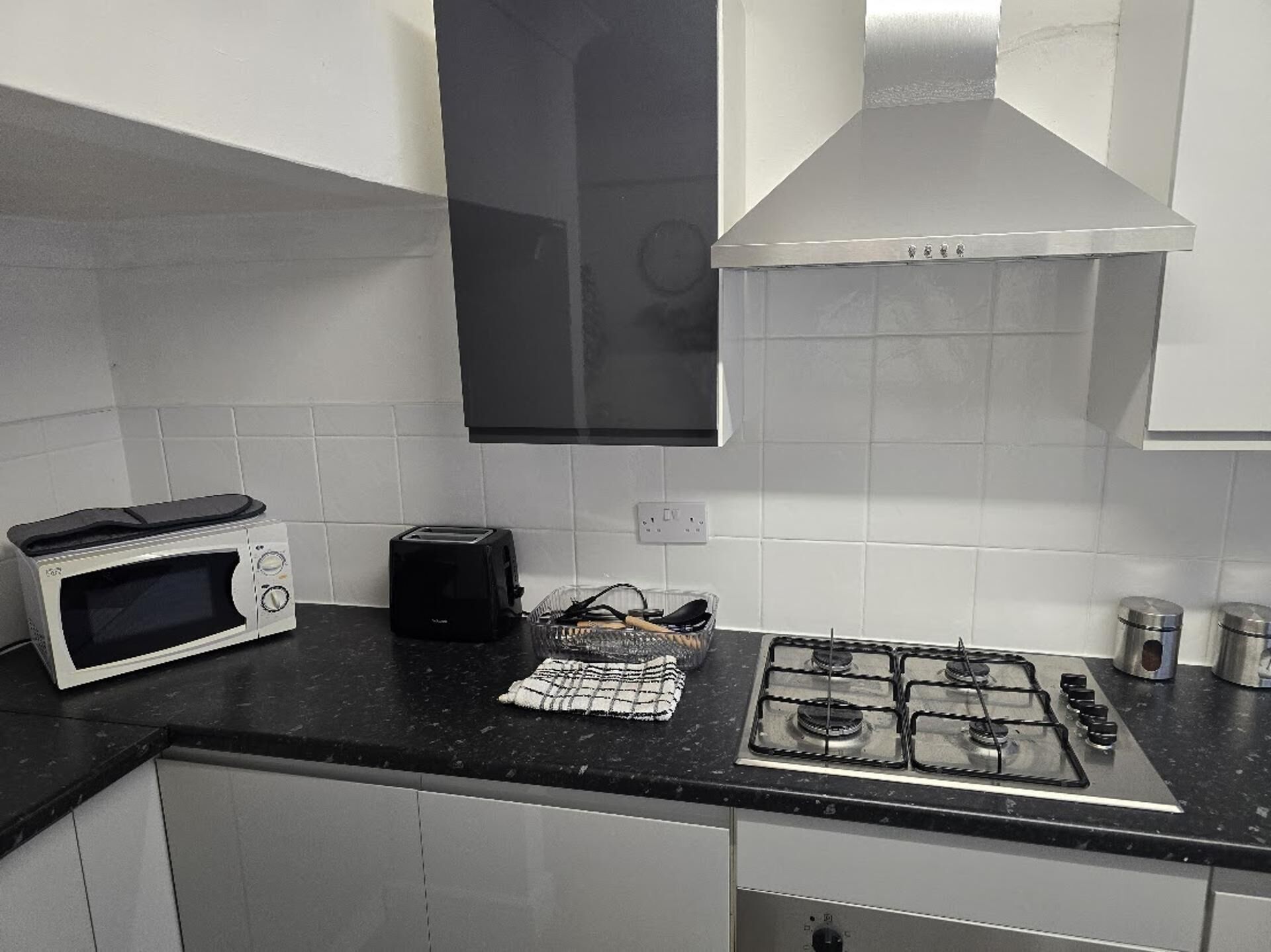 A kitchen with a microwave, toaster, gas stove, and a black range hood.