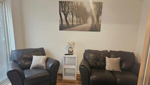 Un salon avec deux canapés en cuir, une petite table d’appoint blanche surmontée d’un vase, et un tableau encadré accroché au mur.