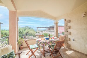 En overdækket terrasse med spiseplads, omgivet af stole, og udsigt over landskabet.