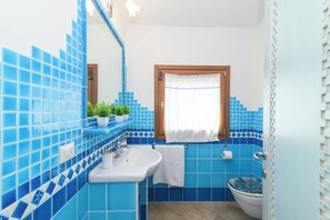 Et badeværelse med blå fliser, en hvid vask, et toilet og et spejl.