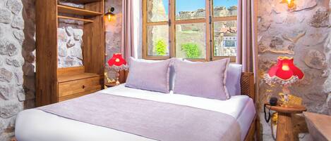 Quarto com cama de madeira, parede de pedra, janela com vista e duas luminárias de cabeceira.