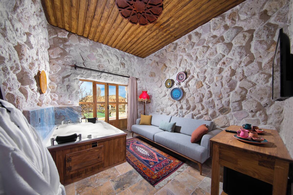 Una habitación con paredes de piedra y techo de madera, una bañera, un sofá, una mesita y un ventanal con vistas.