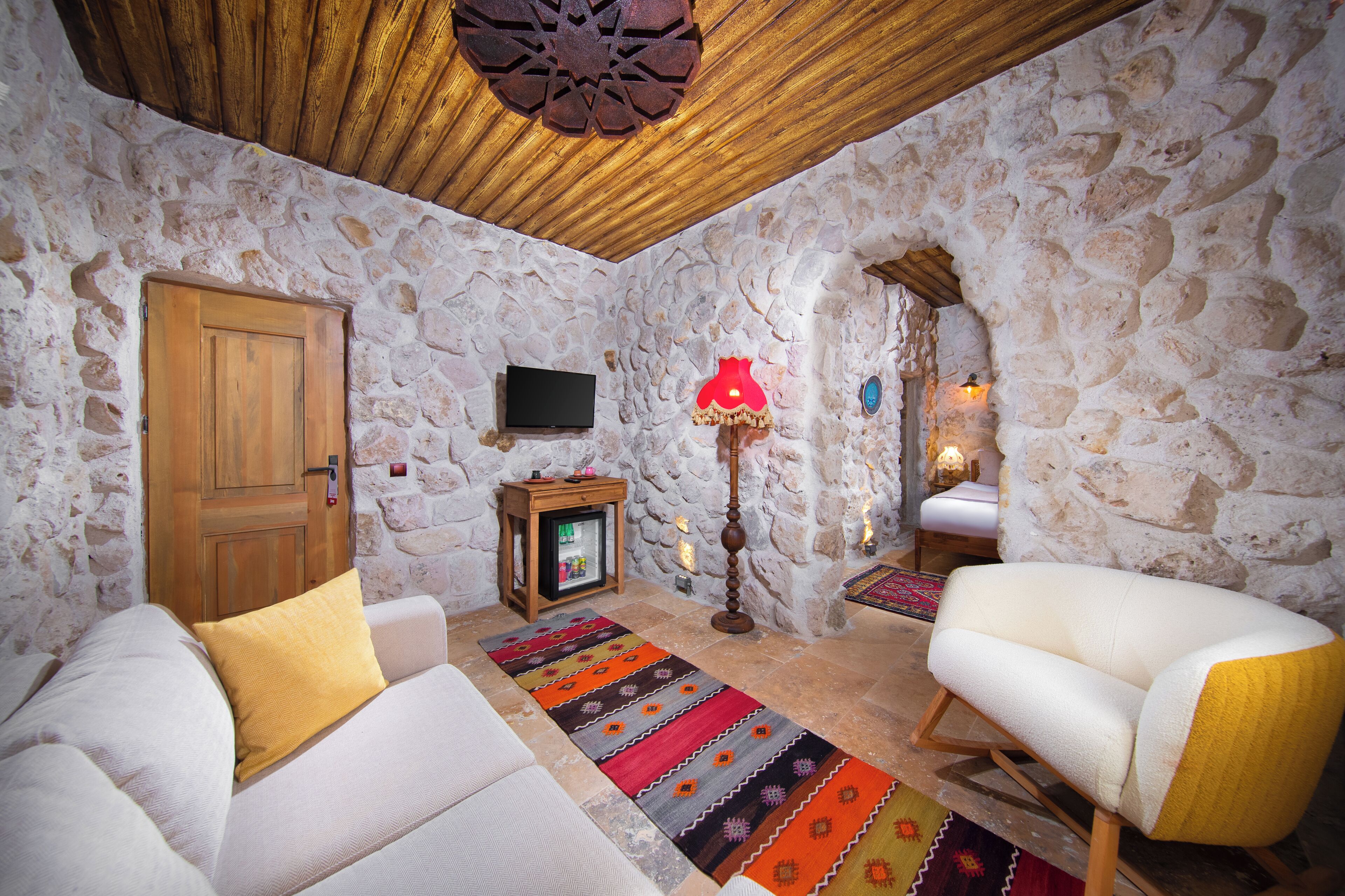 A cozy room with stone walls, a wooden ceiling, a television, a lamp, and two sofas.