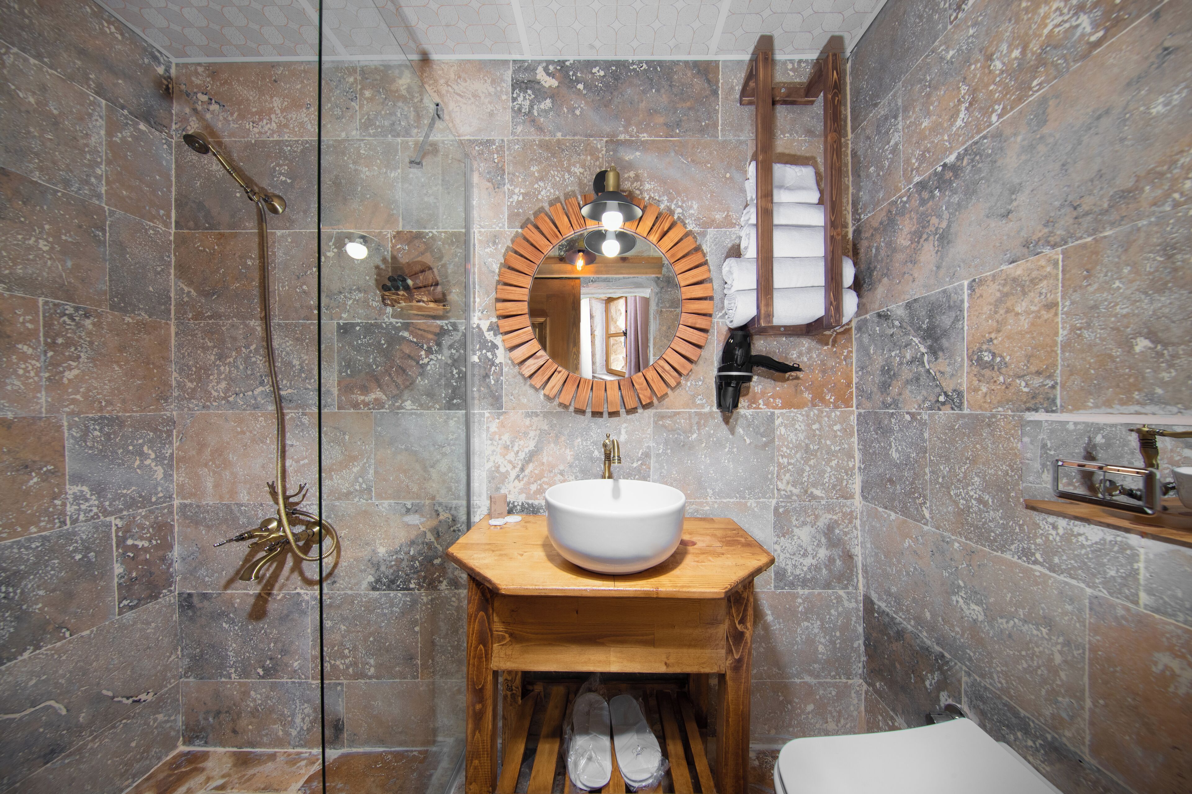 A bathroom with a wooden vanity, a round mirror, a shower, and a towel rack.