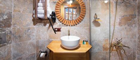 Un baño con tocador de madera, un espejo redondo, un lavabo blanco y una ducha con cabezal dorado.