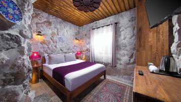 Un dormitorio con paredes de piedra, una cama de madera, una mesita de noche con una lámpara, una cafetera y un televisor sobre una mesa de madera.