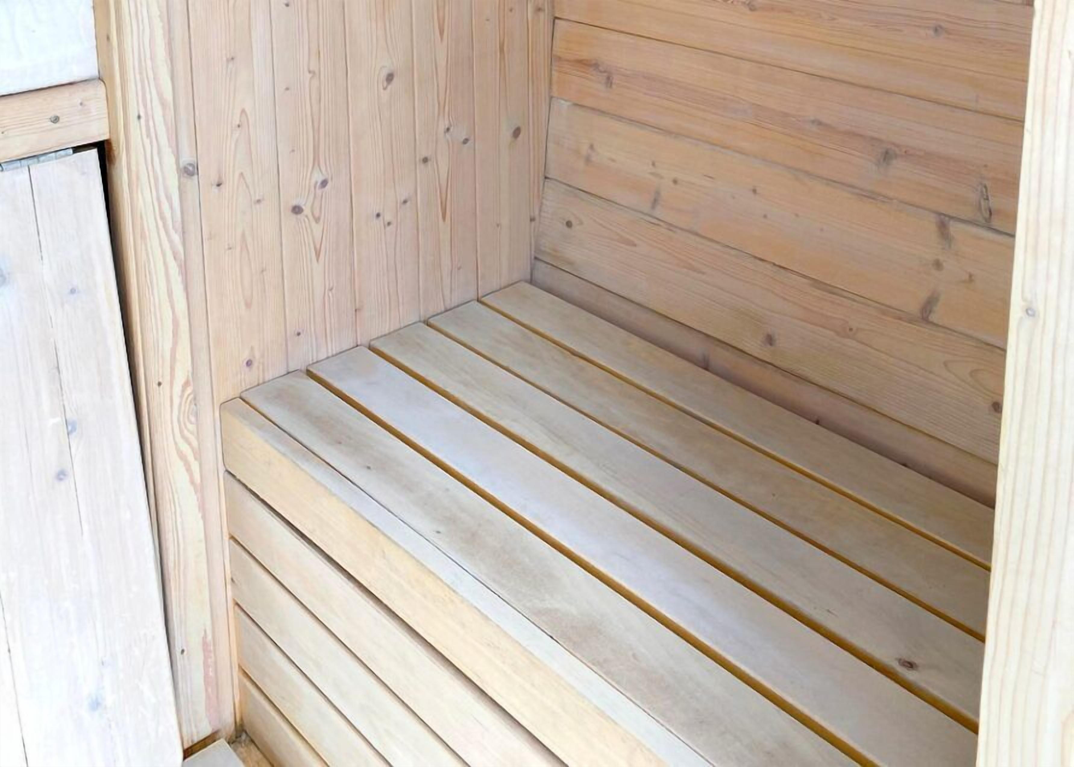 A wooden sauna with a bench and a door.
