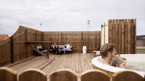 Una terraza exterior de madera con un jacuzzi, sillones de descanso y un cerco de madera.