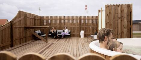 An outdoor wooden deck with a hot tub, lounge chairs, and a wooden fence.