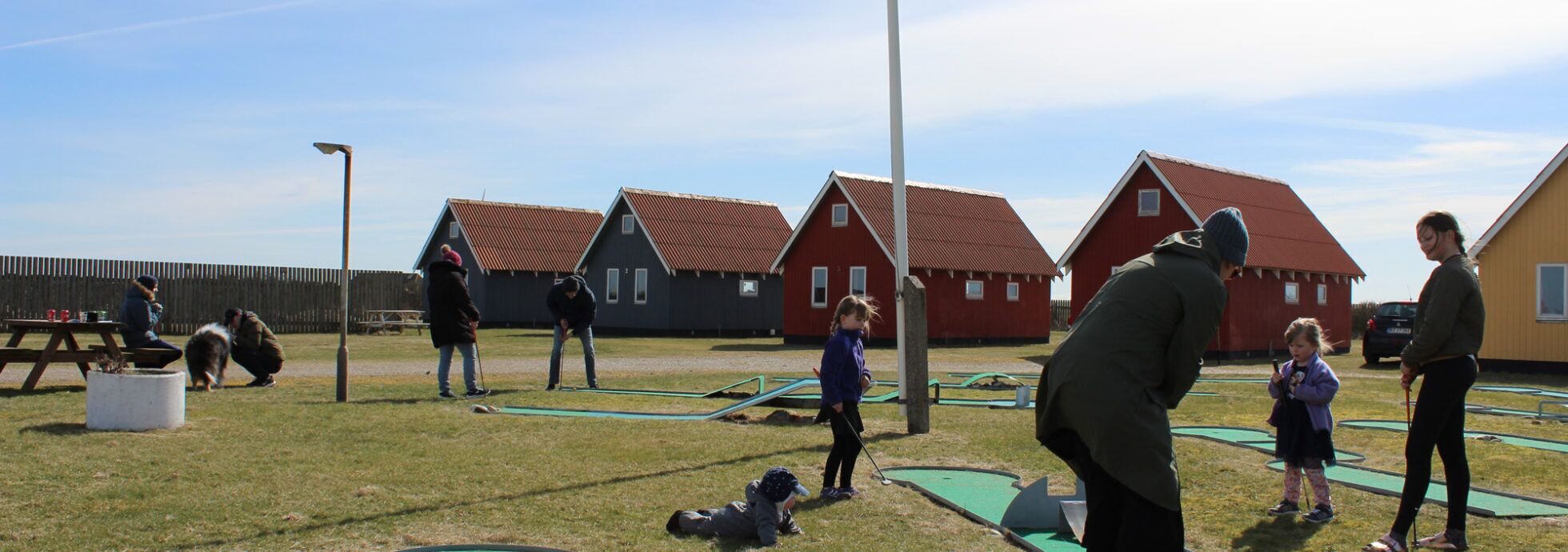 A group of people playing golf in an outdoor setting with houses in the background.