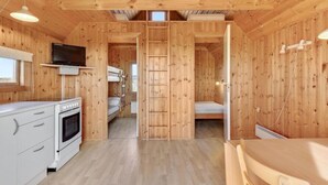 Una cabaña de madera pequeña con kitchenette, una cama individual y un catre en lo alto.