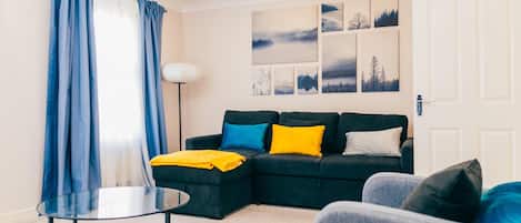 A modern living room with a sectional sofa, a glass coffee table, and a blue and white patterned rug.