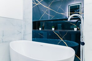 Un baño moderno con una bañera independiente, un tocador con puerta de vidrio y paredes con diseño de mármol.