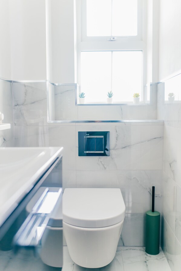 A modern bathroom with a white toilet, a marble backsplash, and a window above the sink.