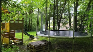 Un terrain de jeux avec un toboggan et un trampoline, le tout entouré d’arbres.