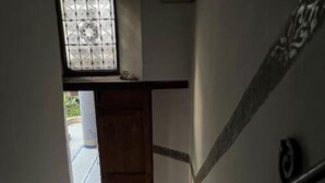 A narrow hallway with a wooden door at the end, a metal railing, and patterned floor tiles. - DAR Benjelloun Studio Plat (Fès)